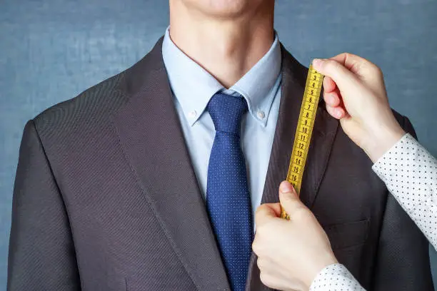 The tailor measures the suit with a measuring tape close up