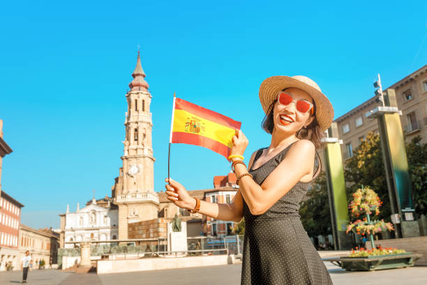 ハッピーアジアの女性旅行者は、サルバドール大聖堂の背景にサラゴサのメイン広場にスペイン国旗と立っています - salvador bahia state travel women ストックフォトと画像