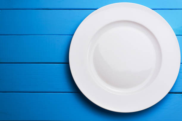 istock White plate and a fork with a spoon on a blue wooden table background. 1144729719