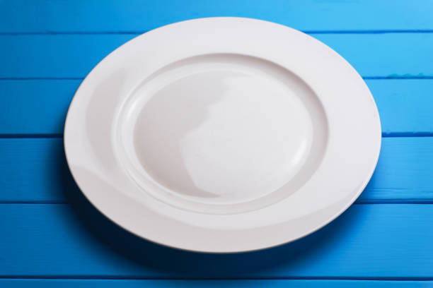 istock White plate and a fork with a spoon on a blue wooden table background. 1144730047