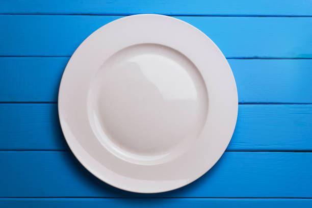 istock White plate and a fork with a spoon on a blue wooden table background. 1144730590