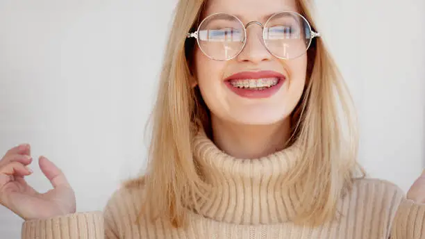 Stylish and beautiful young blonde with glasses and beige oversize sweater. Young woman wearing braces and smiling