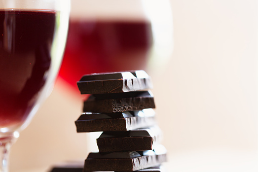 close up of a staple of dark chocolate, glasses with red wine in background