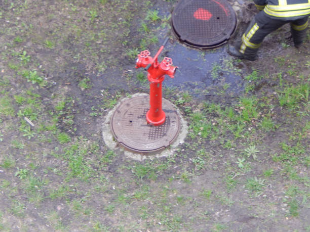 A bright red fire hydrant with white stripes stands prominently in a grassy outdoor area. The soft, blurred background of buildings adds depth to the image, emphasizing safety infrastructure within an urban environment.