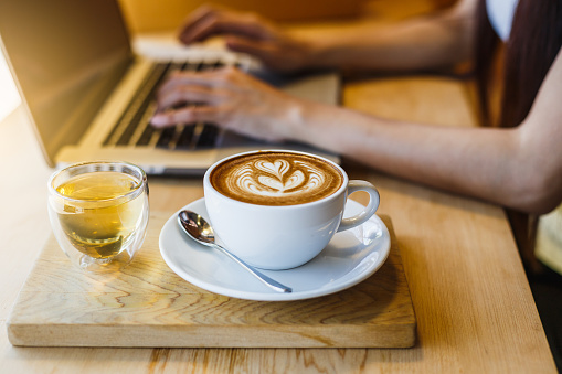 Cropped shot view of business woman or female freelancer using her laptop and working at coffee shop, Selective focus on coffee cup