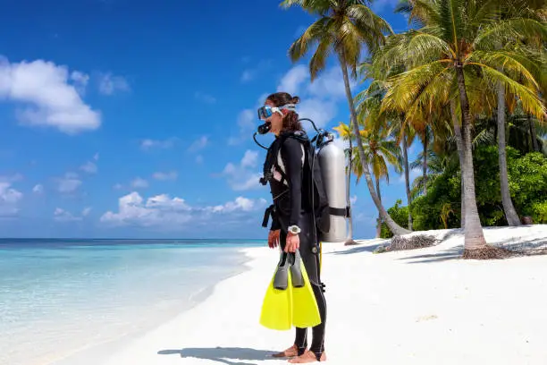 Female scuba diver in full equipment stands on a tropical beach ready to enter the water