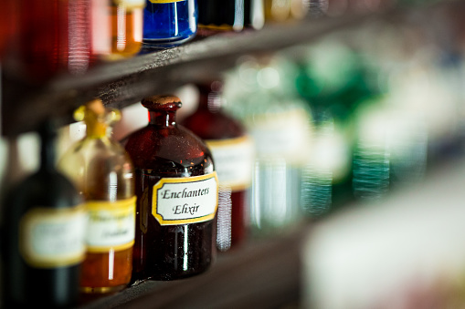 Close up color image depicting glass medicine bottles and vials displayed on wooden shelves in an old fashioned pharmacy. Selective focus on the bottles with plenty of room for copy space.