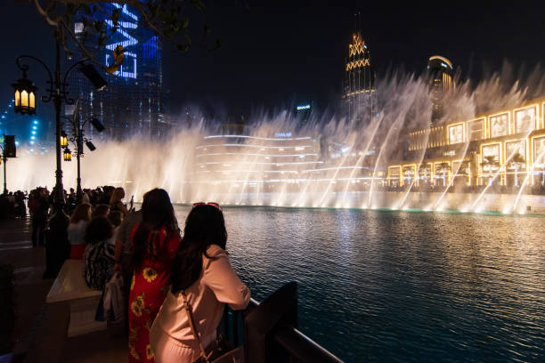 туристы смотрят дубайский торговый центр фонтан шоу ночью в озере бурдж-халифа перед торговым центром - dancing fountains стоковые фото и изображения
