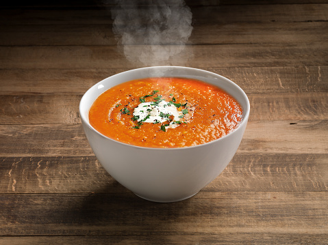Tomato Pomodori soup with herb cream cheese and green herbs in a luxury bowl on a restaurant table. There are no people or trademarks in the shot.