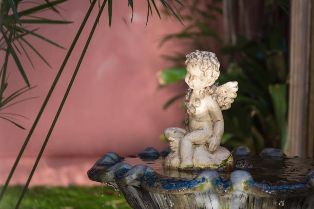 istock Aged white angel Cupid sculpture sitting water fountain. 1144784500