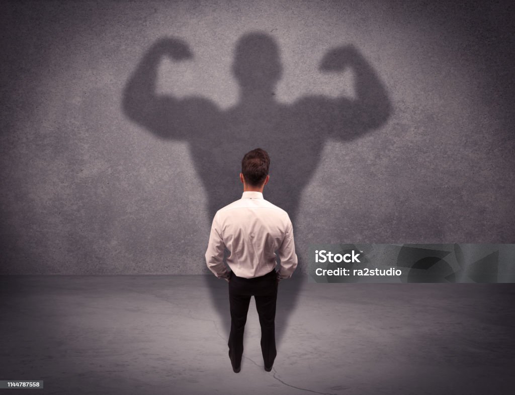 Successful businessman with strong shadow A young salesman standing with his back, looking at his musculous shadow reflecting on the wall concept Shadow Stock Photo