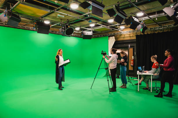 Lights.. Camera.. Action! A wide-angle shot of a multi-ethnic group of people working in a film studio, a mature caucasian woman can be seen presenting in front of a green screen. interview event photos stock pictures, royalty-free photos & images