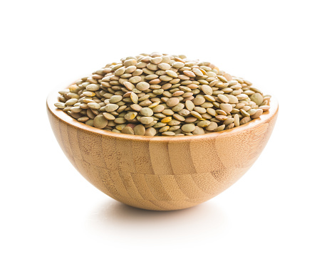 Uncooked dried lentil in wooden bowl isolated on white background.