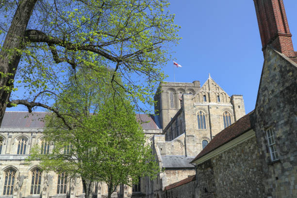 exterior of the stunning winchester cathedral showing the flag of st george fluttering in the breeze on a clear sunny day - uk cathedral cemetery day imagens e fotografias de stock