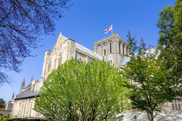 exterior of the stunning winchester cathedral showing the flag of st george fluttering in the breeze on a clear sunny day - uk cathedral cemetery day imagens e fotografias de stock