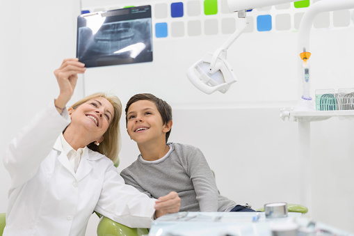 Portrait of a happy dentist looking at an x-ray with a young patient smiling - healthcare and medicine concepts