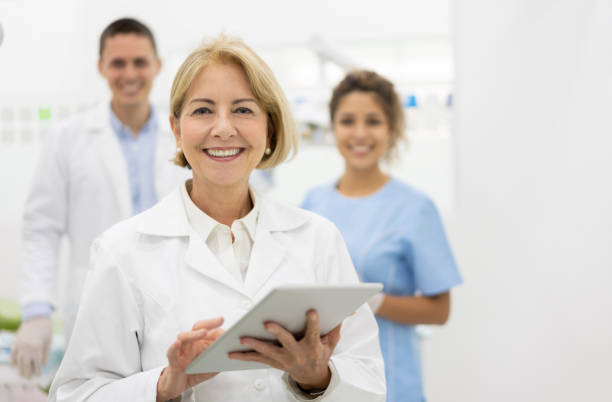 dentiste heureux au bureau avec son équipe et tenant un ordinateur de tablette - healthcare and medicine smiling group of people lab coat photos et images de collection