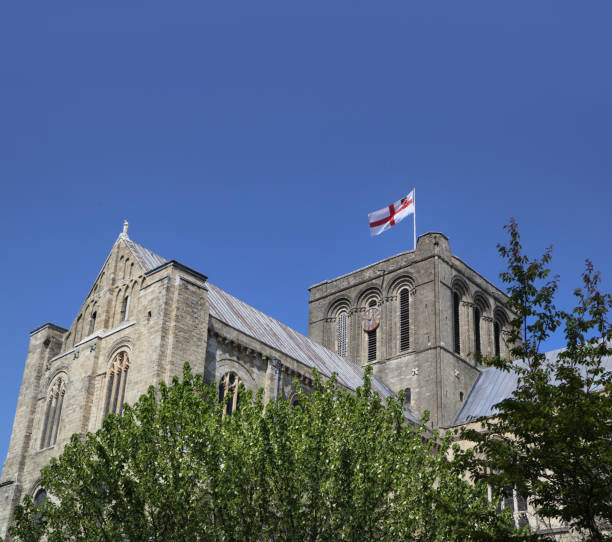 exterior of the stunning winchester cathedral showing the flag of st george fluttering in the breeze on a clear sunny day - uk cathedral cemetery day imagens e fotografias de stock