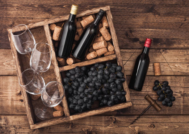 istock Mini bottles of red wine and empty glasses with dark grapes with corks and opener inside vintage wooden box on grunge wooden background. Top view 1144803351