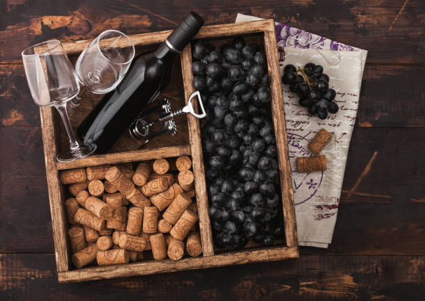 istock Luxury bottle of red wine and empty glasses with dark grapes with corks and corkscrew inside vintage wooden box on dark wooden background with linen towel.Top view 1144803556