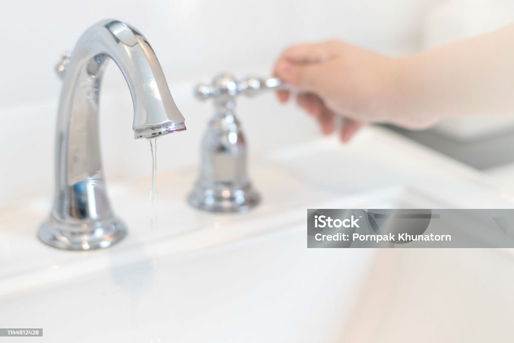 Save the water concept.Hand closing valve on sink in bathroom. Water dripping to stop running as hand turn off the faucet.Detect-a-Leak week. Faucet Stock Photo