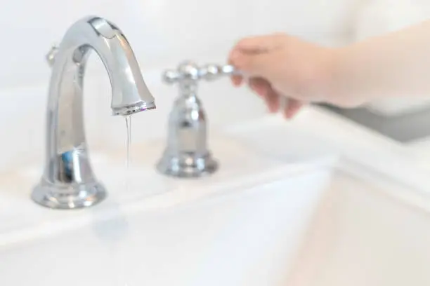 Photo of Save the water concept.Hand closing valve on sink in bathroom. Water dripping to stop running as hand turn off the faucet.Detect-a-Leak week.