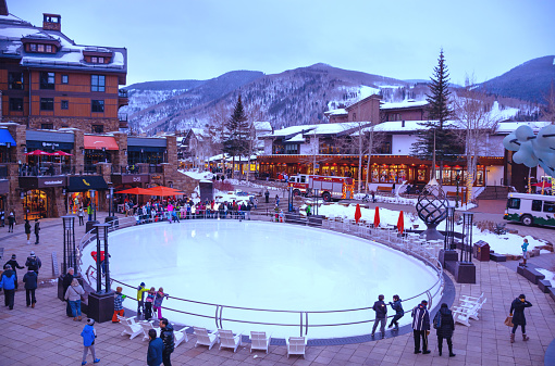 Vail, Colorado/USA-December, 30,2018. Small town at the base of Vail Mountain, gateway for winter sports. People walking on busy streets next to skating rink. Stores and  mountains in the background.