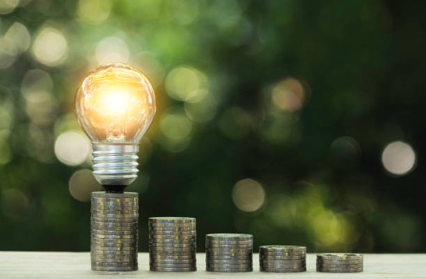 istock Energy saving light bulb  stacks of coins on nature background. 1144815509