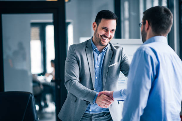Two smiling businessmen shaking hands while standing in an office. Two smiling businessmen shaking hands while standing in an office. business handshake stock pictures, royalty-free photos & images