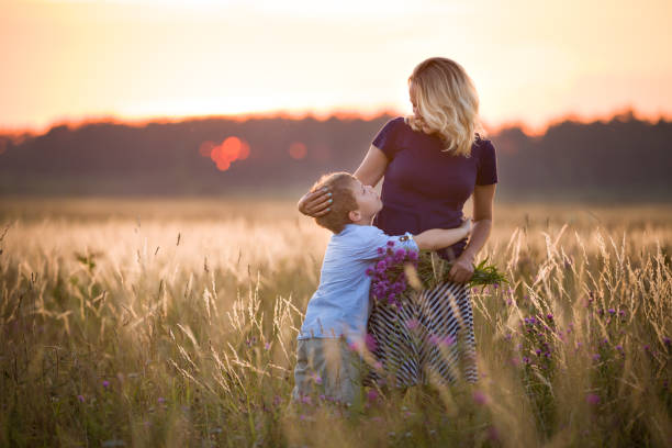 cute kid boy hugging his mother on a summer meadow on beautiful summer sunset. happy family together. mum and child. motherhood and childhood. family walking in the field. outdoors. - child looking blank offspring imagens e fotografias de stock