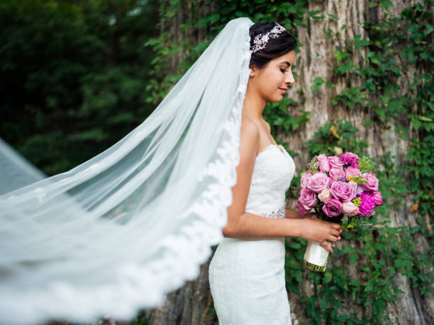 Beautiful latin bride with long veil and bouquet A beautiful young latin bride wearing a long veil and holding a flower bouquet. strapless stock pictures, royalty-free photos & images