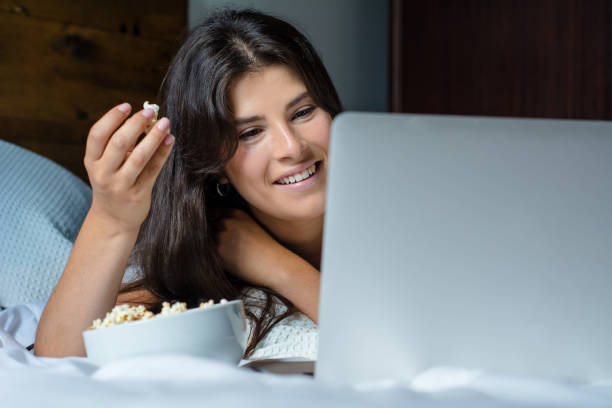 istock Young woman using laptop and eating popcorn 1144830504