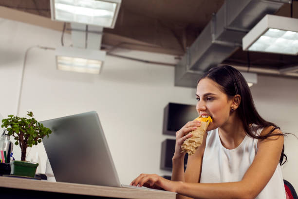 istock Latina woman, concentrated in her work, in front of the computer, while eating a sandwich quickly 1144834066