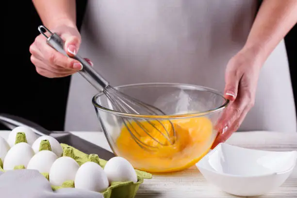 Photo of young woman in a gray aprons breaks the eggs