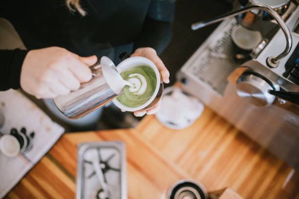 Barista Working At Coffee Shop Espresso Machine A woman works in her small modern coffee shop, enjoying the perfection of her craft coffee beverage preparation. She pours froth art for a customers Matcha green tea latte. matcha tea photos stock pictures, royalty-free photos & images