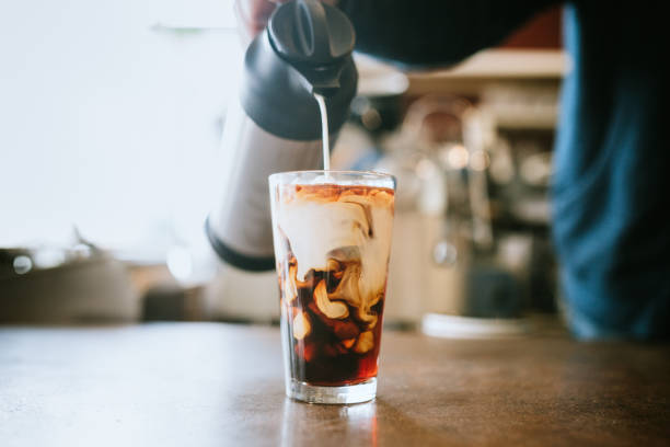 Barista Pours Milk Into Cold Brew Coffee A man pours cold whole milk in to a glass of iced coffee in a cafe.  A cool refreshing drink for a hot summer day. iced coffee stock pictures, royalty-free photos & images