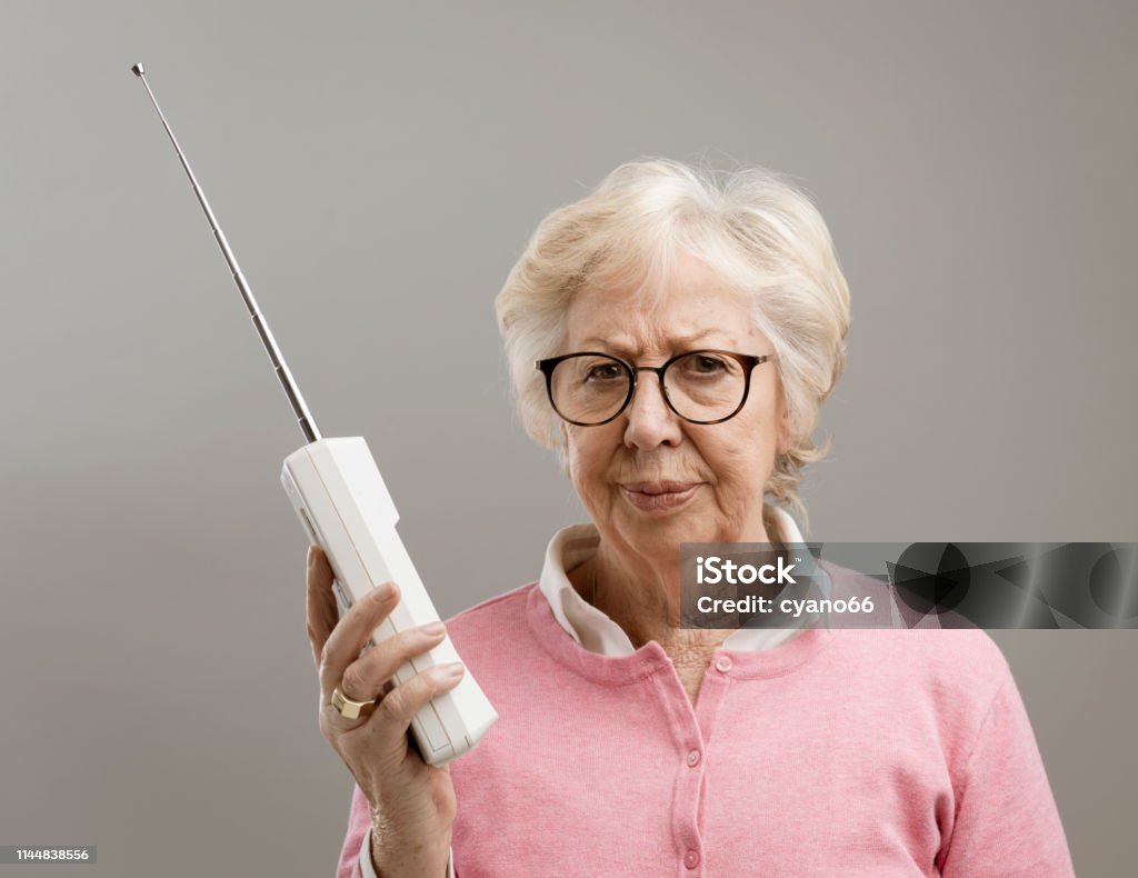 Frustrated senior woman using an old telephone Frustrated senior woman using an old cordless telephone, she is looking at camera disappointed Anger Stock Photo