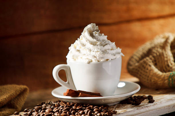 Black coffee cup on wooden background with coffee beans, cinnamon sticks. Hot drink coming out smoke