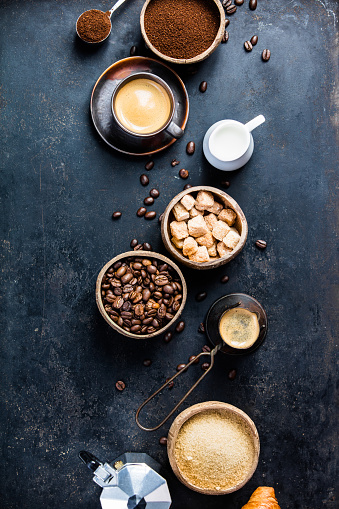 Coffee composition on dark background. Coffee espresso in dark cups, coffee beant, ground coffee, brown sugar, milk, croissants, capsules. Breakfast concept. Flat lay