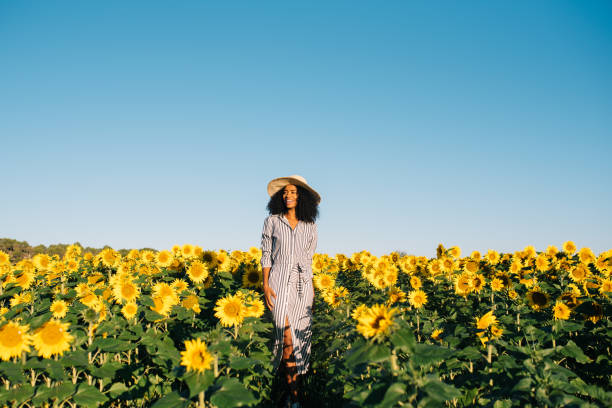 jeune femme noire heureuse marchant dans un champ de tournesol - women dress black young women photos et images de collection