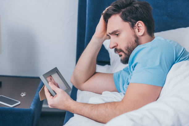 istock upset man lying in bed, touching head and holding photo frame at home 1144866062