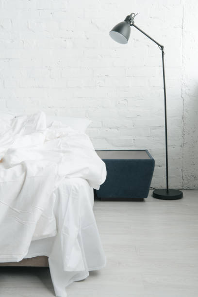 istock Bed with white sheets and blanket, lamp and black nightstand 1144867615