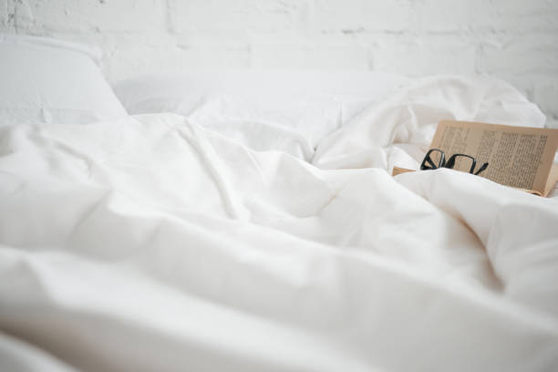 istock Selective focus of book with glasses on white bed 1144867643