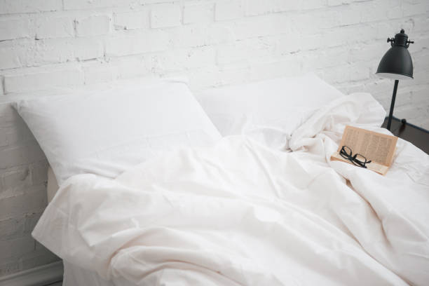 istock glasses and book on bed with white blanket and pillows, lamp 1144867662