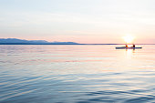 People women sea kayaking paddling boat in calm water together at sunset. Active outdoor adventure water sports. Journey, destination, teamwork concepts.