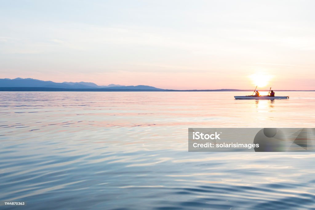 People women sea kayaking paddling boat in calm water together at sunset. Active outdoor adventure water sports. Journey, destination, teamwork concepts. Kayak Stock Photo