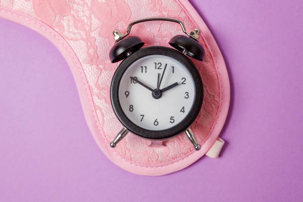 istock Sleeping mask and alarm clock on purple violet background 1144870909