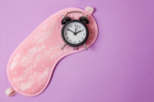 istock Sleeping mask and alarm clock on purple violet background 1144870993
