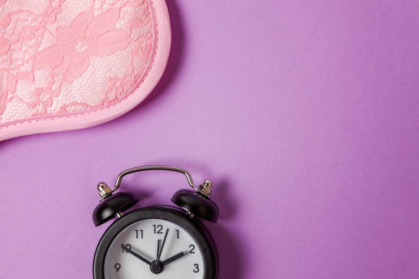 istock Sleeping mask and alarm clock on purple violet background 1144871748