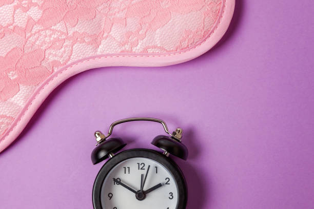 istock Sleeping mask and alarm clock on purple violet background 1144871768
